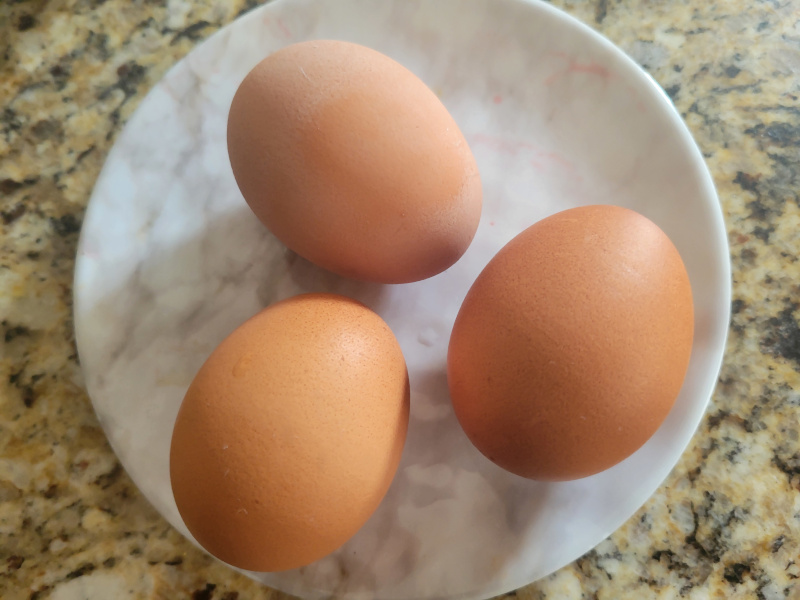 Three raw eggs cracked into a white plate, with bright yellow yolks intact, ready to be scrambled for breakfast